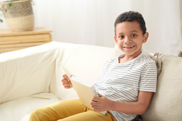 Little African-American boy with hearing aid reading book at home