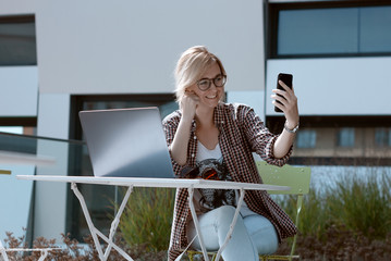 Beautiful woman taking selfie on her smartphone during the work break. Blogger freelancer with...
