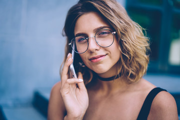 Prosperous millennial hipster girl in trendy sunglasses making positive friendly telephone call via application on cellphone, close up portrait of smiling woman talking with colleague via cellular