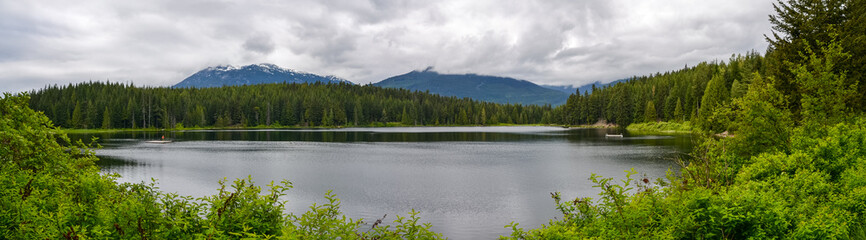 A view through the pine forest towards the snow capped mountains beyond the lake on a cloudy day.