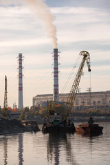 Industrial landscape. River, pipes with smoke and factory. Crane on a barge loads cargo. Smokes from pipes. Industrial area near the river. Cityscape Scenery.