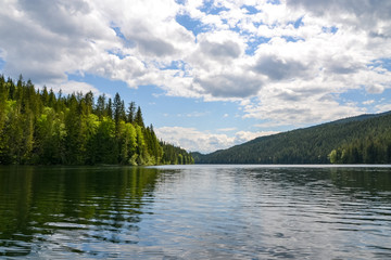 The dense pine forest lining the edges of Clearwater Lake reflects on the rippled water. The clouds and trees reflect on the surface of the lake on this calm and sunny day.