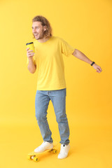 Portrait of happy man with skateboard and cup of coffee on color background