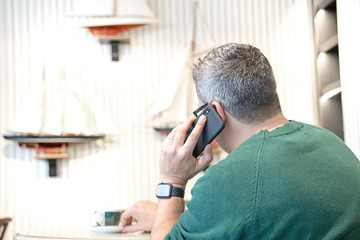 Man with using smartphone talking at coffee shop cafe from back view