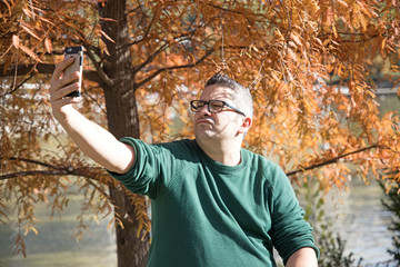 Portrait of a man taking a selfie while standing in front of an orange lighted tree.