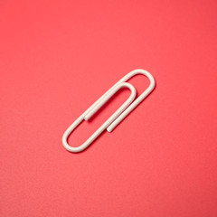 One white paper clip on a pink background. Flat layout