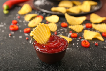 Tasty sauce and potato chips on dark background