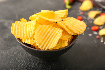 Bowl with tasty potato chips on dark background