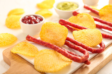 Tasty potato chips, smoked sausages and sauces on light background