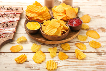 Tasty potato chips and bacon on light wooden background