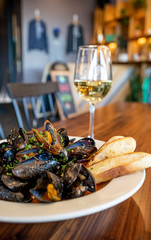 Mussels Steamed in White Wine Garlic Saffron Broth with Glass of Wine and Grilled Bread Up-Close on a White Plate