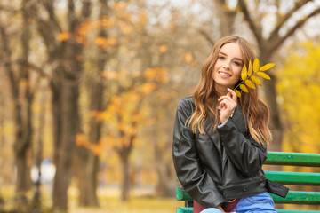 Portrait of stylish young woman sitting on bench in autumn park