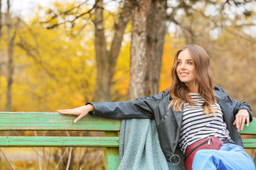 Portrait of stylish young woman sitting on bench in autumn park