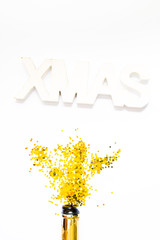 Creative photo of champagne bottle with confetti on white  background with a giant xmas decoration on top, . Flat lay of christmas, anniversary, new year celebration concept.