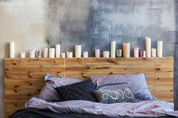 Stylish bedroom in loft style with grey colors and many candles. Bed with dark grey blanket