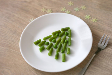 Edible Christmas tree made of peas and green beans on wooden background. Nice way to serve vegetables. Vegan Christmas menu