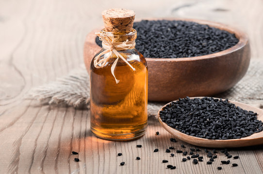 glass bottle of black cumin seeds essential oil , Nigella Sativa in spoon on wooden background. Organic herbal medicine for many diseases, texture background