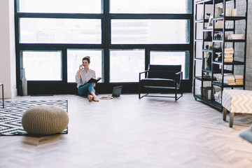 Happy skilled woman smiling and resting on apartment floor and calling to friend for consultancy about university course work using mobile application and 4g internet during learning at home interior