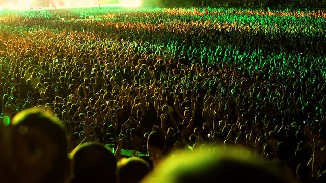 Music concert. A crowd of unrecognizable people applauding, dancing, jumping, raising their hands up, watching performance of a musical group on stage of music hall. 4K