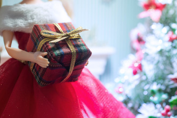 Doll holding a gift box with gold ribbon.