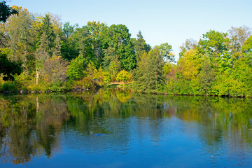 Fototapeta na wymiar Small lake in Duke Farms, New Jersey, lined with trees sporting early autumn colored leaves