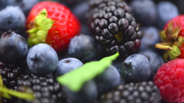 Berries. Various colorful berries background. Strawberry, raspberry, blackberry, blueberry closeup over black. Healthy eating. Rotation. Slow motion 4K UHD video footage. 3840X2160