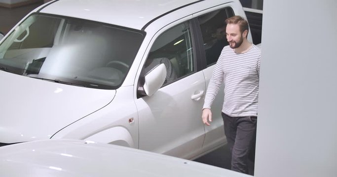 Top view of bearded Caucasian man examining white pickup in car dealership. Male trader reflecting in car surface. Successful businessman choosing automobile. Car business. Cinema 4k footage ProRes HQ