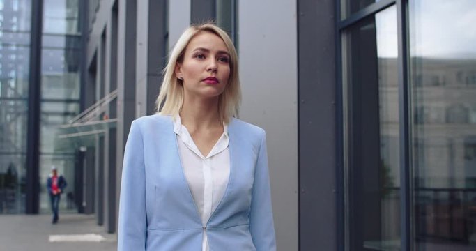 Pretty young Caucasian blonde businesswoman in stylish outfit walking outdoor while going to the office at modern building. Heading to the meeting.