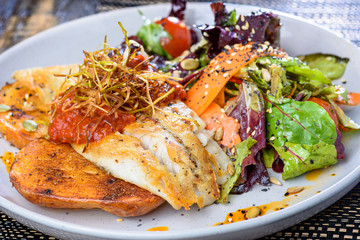 A serving of grilled fish with vegetables and salad