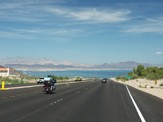 Biker travellking to Lake Mead by Nevada road, mountain range in background on sunny day