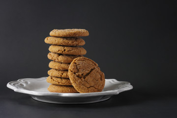 A stack of chewy ginger cookies on a white plate and a black background