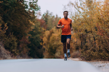 Fototapeta premium Male runner jogging and running on road in nature landscape