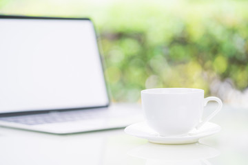 Coffee cup and laptop at office with bokeh