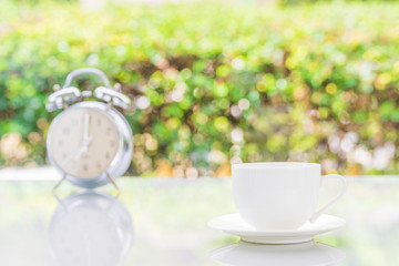 Silver alarm clock and white coffee cup