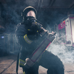 Portrait of a female firefighter wearing a helmet and all safety equipment a while holding a...