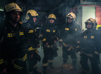 Team of firefighters standing inside ( indoors ) a buliding next to a fire engine.