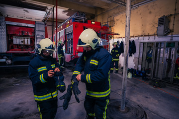 Firefighters preparing their uniform and the firetruck in the background inside the fire station