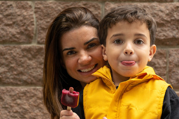 Smiling mother behind her son holding a popsicle with yellow vest .