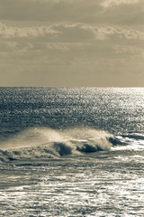 Grey and blue stylized view of ocean wave crashing and rolling in on a bright day
