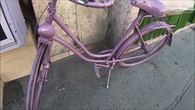 Girly bicycle painted all purple is standing in front of a house, recorded from hand, fish eye perspective