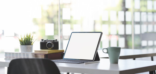 Comfortable office room with mock up digital tablet, camera and office supplies with sunlight in the background