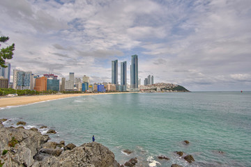 Naklejka premium Scenic view of awesome rocky beach, sea and skyscrapers in Busan in South Korea. Beautiful summer cloudy look of relax place in resort city of Republic of Korea