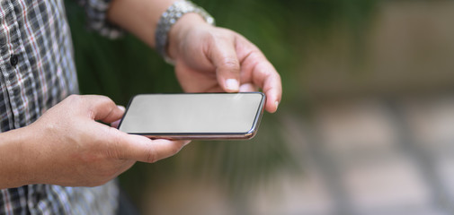 Close-up view of professional businessman using mock up smartphone with outdoor office background