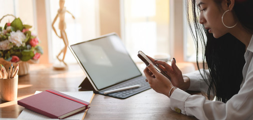 Cropped shot of young businesswoman working on her project while using smartphone in comfortable office