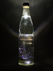 Glass bottle with drink and backlight on black background.