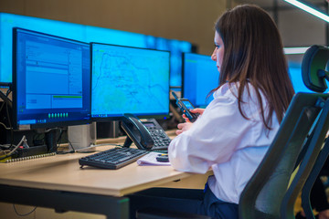 Female security guard sitting and monitoring modern CCTV cameras in a surveillance room.