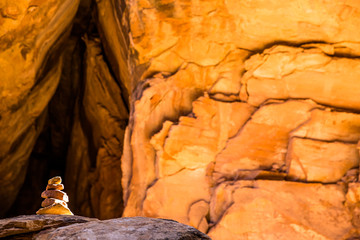 Cairn in bright orange sandstone slot canyon lit by narrow band of sunlight from above.