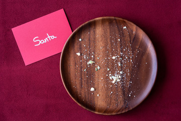 Christmas note to Santa, sugar cookie crumbs on a wood plate, red background