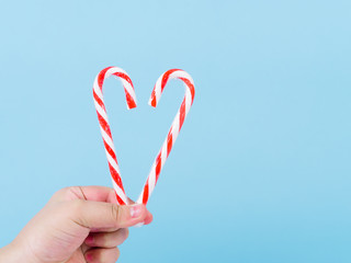 Hand holding Heart shape Christmas candy stick on blue background.