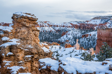 Sandstone tower in beautiful evening light peeking through winter storm clouds after fresh snow.
